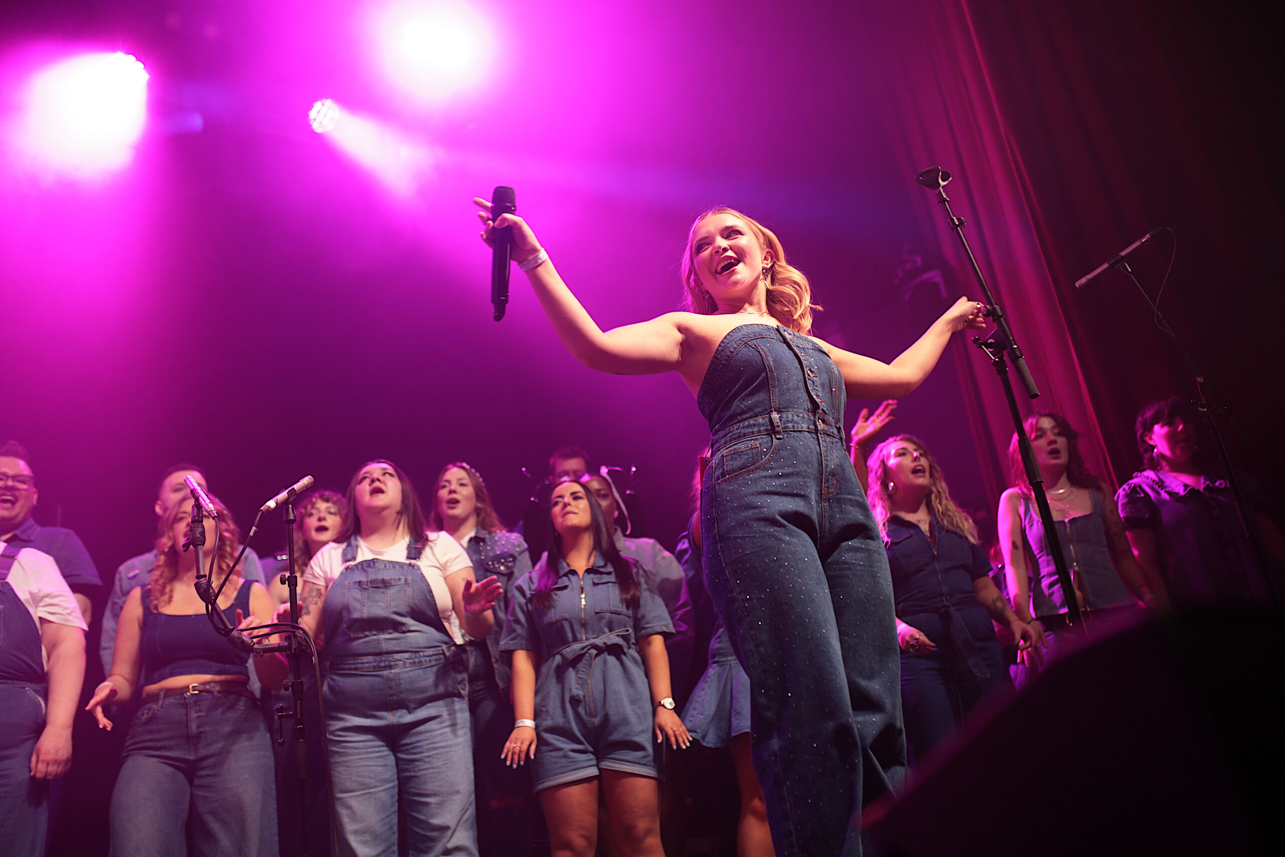 Singers on stage with Groove Chorus lit by pink stage lights.