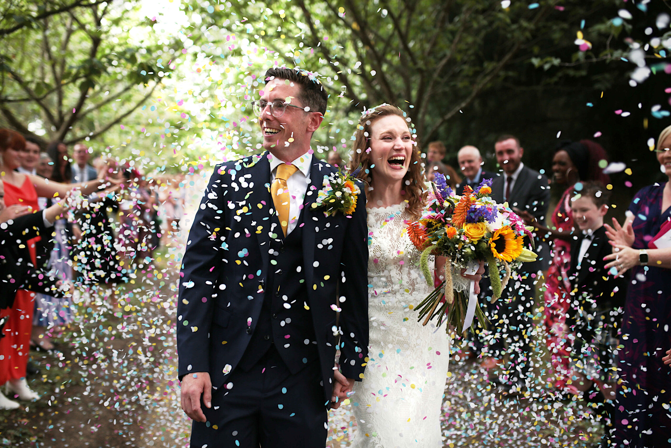A bride and groom laughing as they walk through a confetti throw